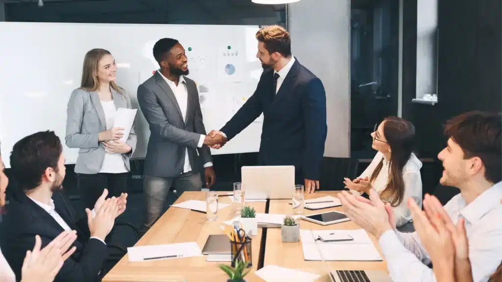 A business meeting ending in teams smiling and shaking hands drawing the meeting to a successful conclusion.